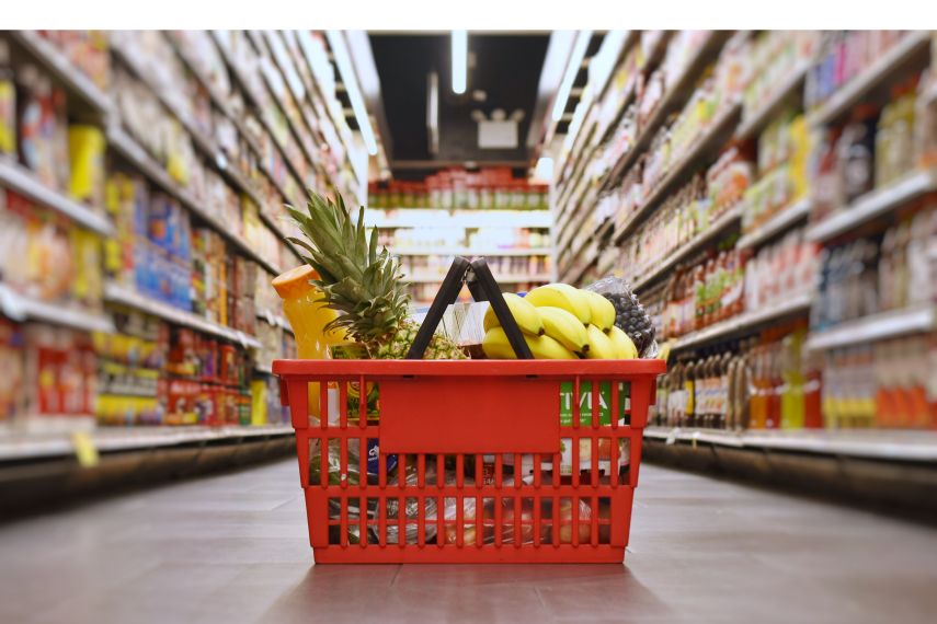 Gefüllter Einkaufskorb steht im Gang zwischen zwei Regalen im Supermarkt